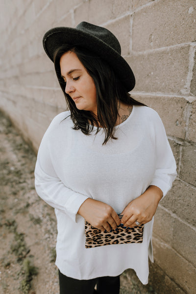 Closeup of Anna standing next to a cinder block wall wearing a plus ivory high low slouchy sweater with 3/4 sleeves.